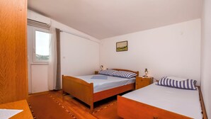 Ein Schlafzimmer mit zwei Holzbetten, einem kleinen Tisch, einem Fenster mit Vorhängen und einem an der Wand hängenden Gemälde.