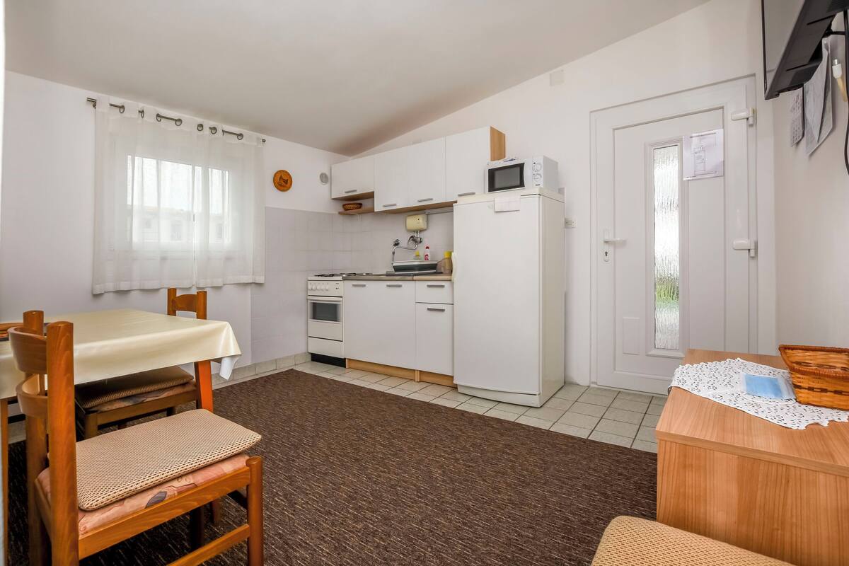 A compact kitchen with white cabinets, a microwave, and a sink. There is a dining table with chairs and a small wooden table with a basket.