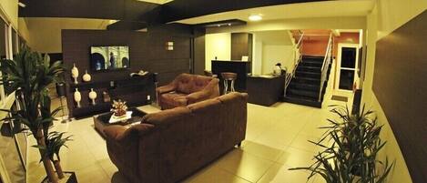 A spacious living area with a sofa, a coffee table, and potted plants. There is a staircase leading to an upper level.