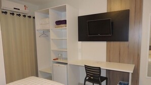 Un dormitorio con cama, escritorio, silla, televisor y armario.