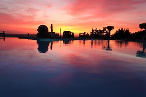 A serene sunset over a swimming pool with a clear sky, calm water, and distant trees.