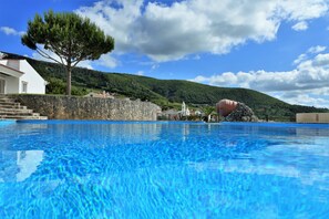 Una piscina con agua azul cristalina, un muro de piedra y un árbol al fondo.