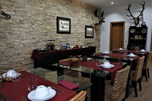 A dining area with a stone wall, framed pictures, and antler decorations. Tables are set with white plates and red napkins.
