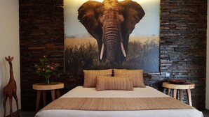 Ein Schlafzimmer mit einem großen Bett, einer Giraffenskulptur, einem Elefantenbild an der Wand und einer Steinwand.