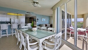 A spacious dining area with a glass table and white wicker chairs, a ceiling fan, and a view of the outdoor patio through large sliding glass doors. - Perfect for Large Family or 2 families, Oceanfront w Ocean Views Heated Pool (New Smyrna Beach)