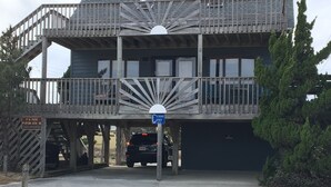 A two-story wooden building with a balcony, a parking area, and a sign indicating a visitor center. - Ocean Views at Cochran’s Corner! (Kill Devil Hills)