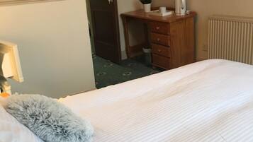 A hotel room with a bed, a wooden dresser, a radiator, and a door.