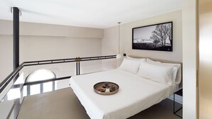 Una habitación de hotel moderna con una cama grande, una bandeja redonda con objetos, un cuadro enmarcado en la pared y un balcón con barandilla.
