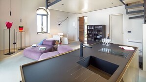 Una cocina moderna con una isla central, un comedor con sofá y sillas, y una escalera que lleva a un nivel superior.