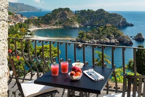 Un balcon avec une table dressée pour deux personnes, offrant une vue sur un paysage côtier avec des affleurements rocheux et une plage.