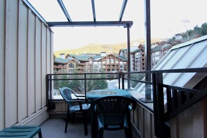 Un balcón con mesa y sillas, con vistas a una montaña y edificios.