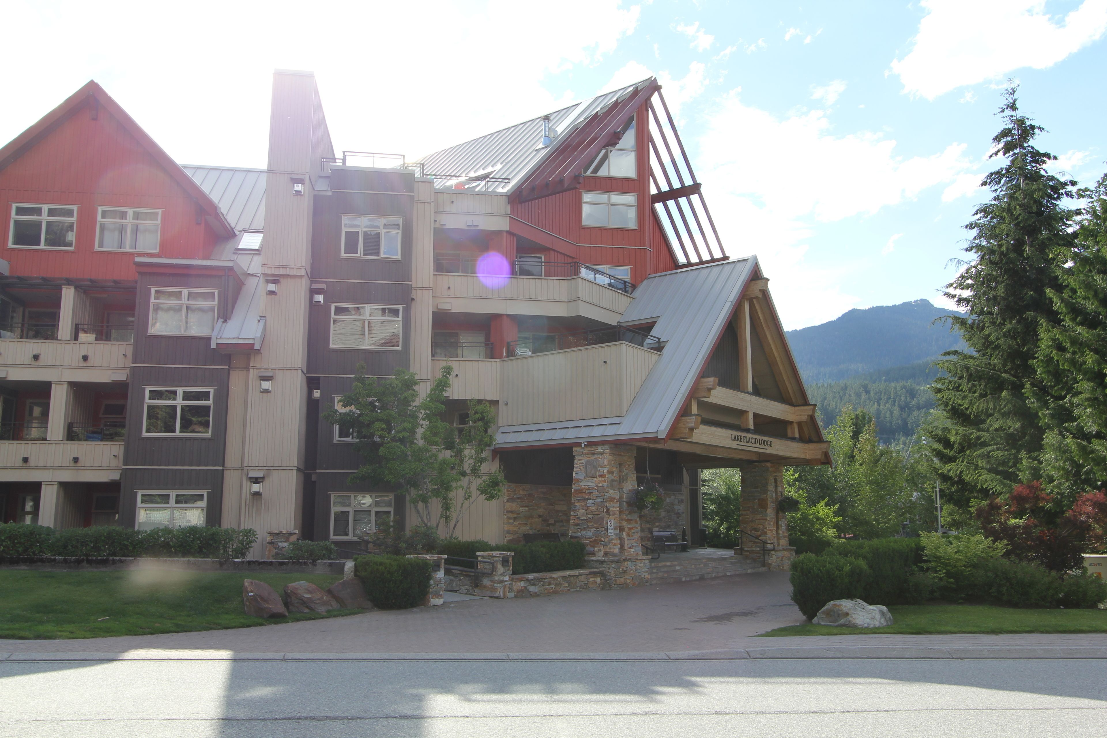 A multi-story building with a sloped roof, stone foundation, and a covered entrance.