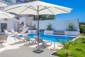 A poolside area with lounge chairs, umbrellas, and a modern architectural design. - Villa Andrea (Punat)