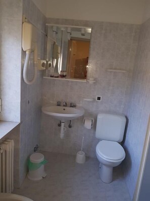 A compact bathroom with a pedestal sink, toilet, and a small trash bin.
