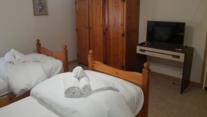 A bedroom with two single beds, a wooden wardrobe, a desk with a television, and a framed picture on the wall.