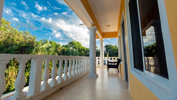 A covered balcony with white balustrades, a bench, and columns. - Nicol-Haa (Izamal)