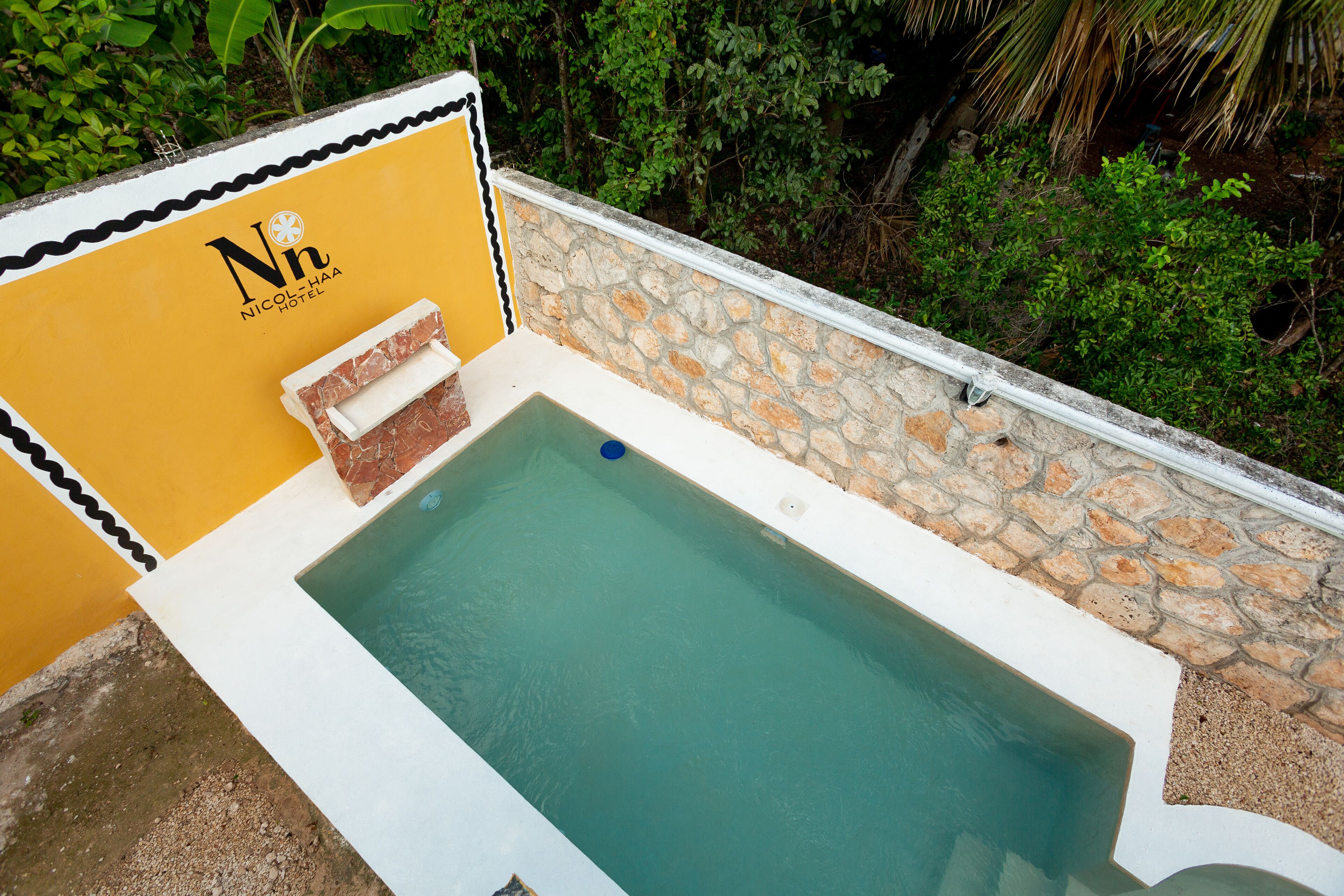 A rectangular pool with a stone wall and a yellow wall with the hotel name.