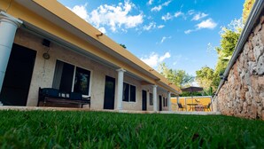 A building with a yellow facade, columns, and a grassy area in the foreground. - Nicol-Haa (Izamal)