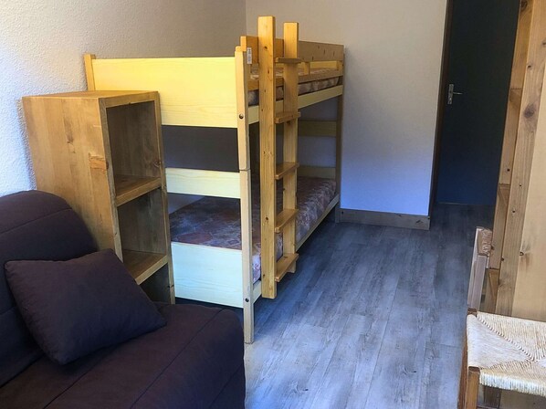 Quarto compacto com uma cama beliche, um sofá e uma porta.