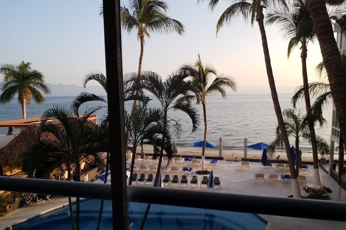 Un espace aménagé au bord de la piscine, avec des chaises longues et des parasols, des palmiers et une vue sur la mer.