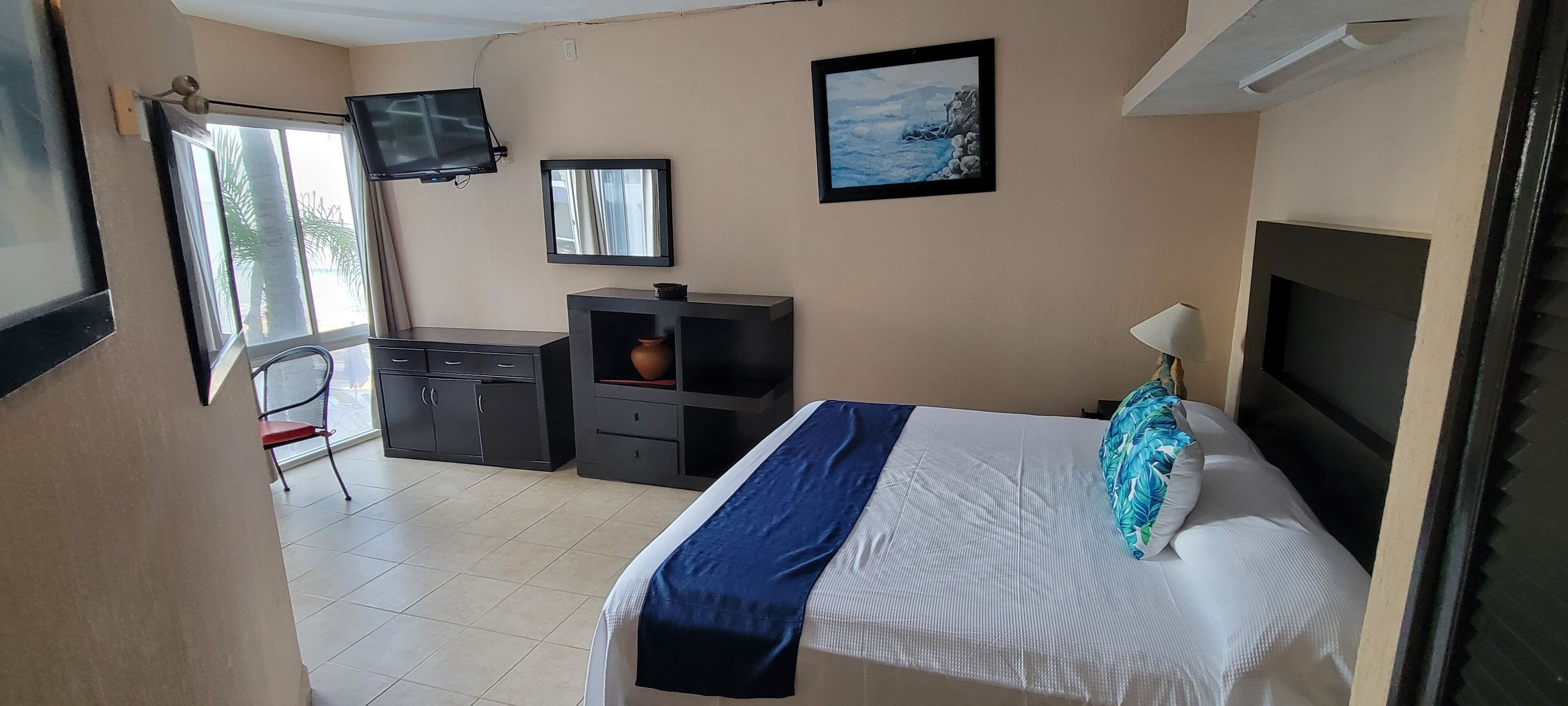 Un dormitorio con cama, escritorio, silla, televisor y ventana.