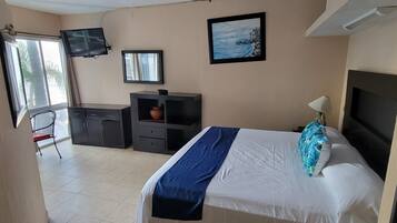 Un dormitorio con cama, escritorio, silla, televisor y ventana.