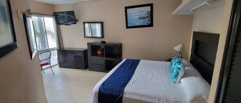 A bedroom with a bed, a desk, a chair, a TV, and a window.