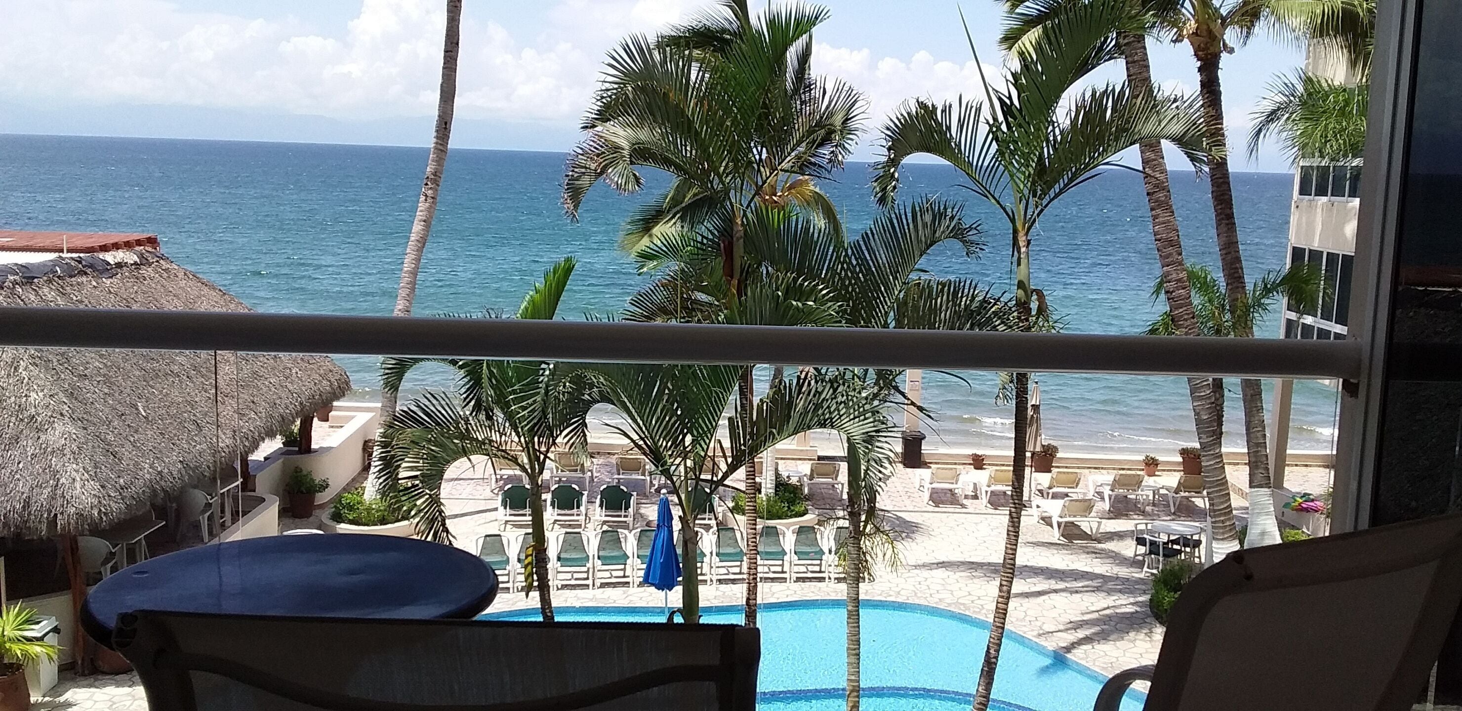 A balcony with a view of a pool, lounge chairs, and palm trees.
