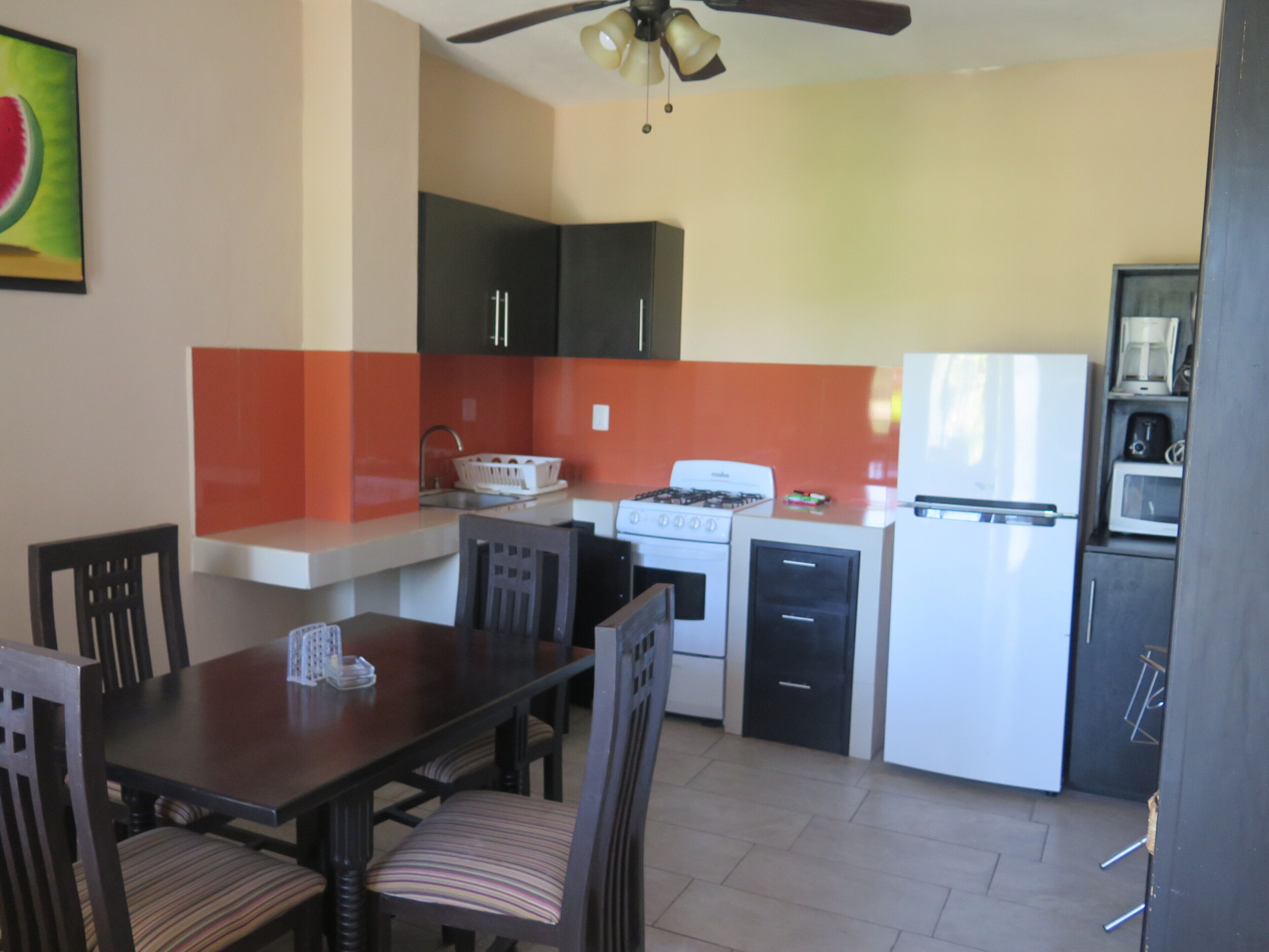 A compact kitchen with a dining table, chairs, a stove, a refrigerator, and a microwave.