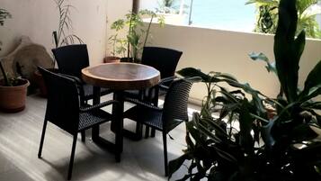 Une table ronde en bois, entourée de quatre chaises en osier noir, et agrémentée de plantes en pot, sur un balcon offrant une vue sur la mer.