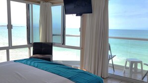Una habitación con cama, una silla, televisión y balcón con vistas al mar.