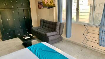 Una habitación con cama, sofá, televisión, armario y ventana con cortinas.