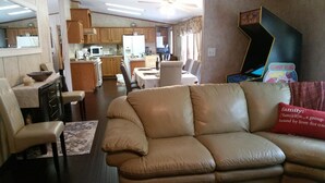 A living room with a beige leather sofa, a dining area with wooden cabinets, and a kitchen with wooden cabinets and appliances. - Catskills Modern Comfort Home Mountainous Backdrop (East Branch)