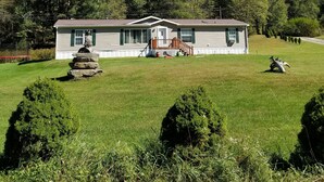 A single-story house with a front porch, a stone sculpture, and a well-maintained lawn. - Catskills Modern Comfort Home Mountainous Backdrop (East Branch)