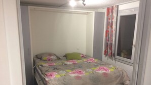 Een eenpersoonsbed met een bloemenprint deken, een groen kussen en een wit hoofdbord in een kamer met een raam en gordijnen.