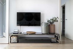 A modern living room with a flat-screen TV mounted on the wall, a glass coffee table, a potted plant, and a wicker basket.
