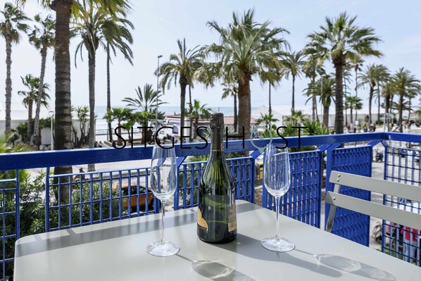 A table with a bottle of wine and two glasses on a balcony overlooking palm trees and the sea. - 20 meters from the beach (Sitges)