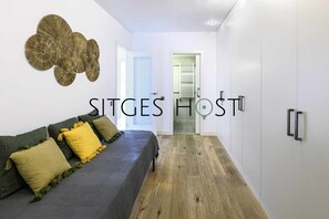 A modern hotel room with a grey sofa, yellow and green pillows, a wooden floor, and a white wall with a decorative wall art piece. - 20 meters from the beach (Sitges)