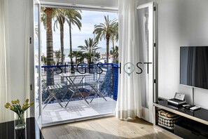 Ein Hotelzimmer mit Balkon, Fernseher, Schreibtisch und Blick auf Palmen und Meer.