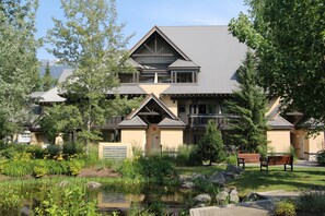 A two-story building with a symmetrical roof design, surrounded by a landscaped garden with a pond and benches. - Lagoons Condos by Whistler Retreats (Whistler)