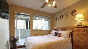 A bedroom with a bed, a dresser, a lamp, a wall decoration, and a window. - Lagoons Condos by Whistler Retreats (Whistler)