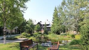 A park with two wooden benches, a pond, and a building with a sloped roof in the background. - Lagoons Condos by Whistler Retreats (Whistler)