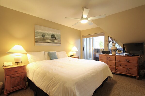 A bedroom with a large bed, two bedside tables with lamps, a ceiling fan, a dresser, and a television. - Lagoons Condos by Whistler Retreats (Whistler)