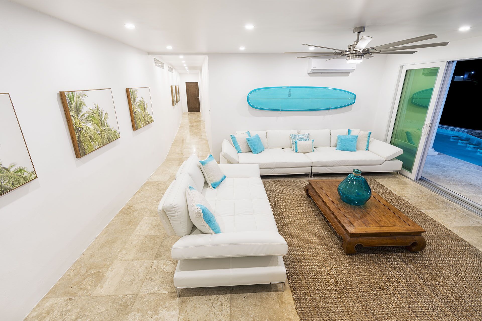 A modern living room with a white sofa set, a wooden coffee table, and a ceiling fan.