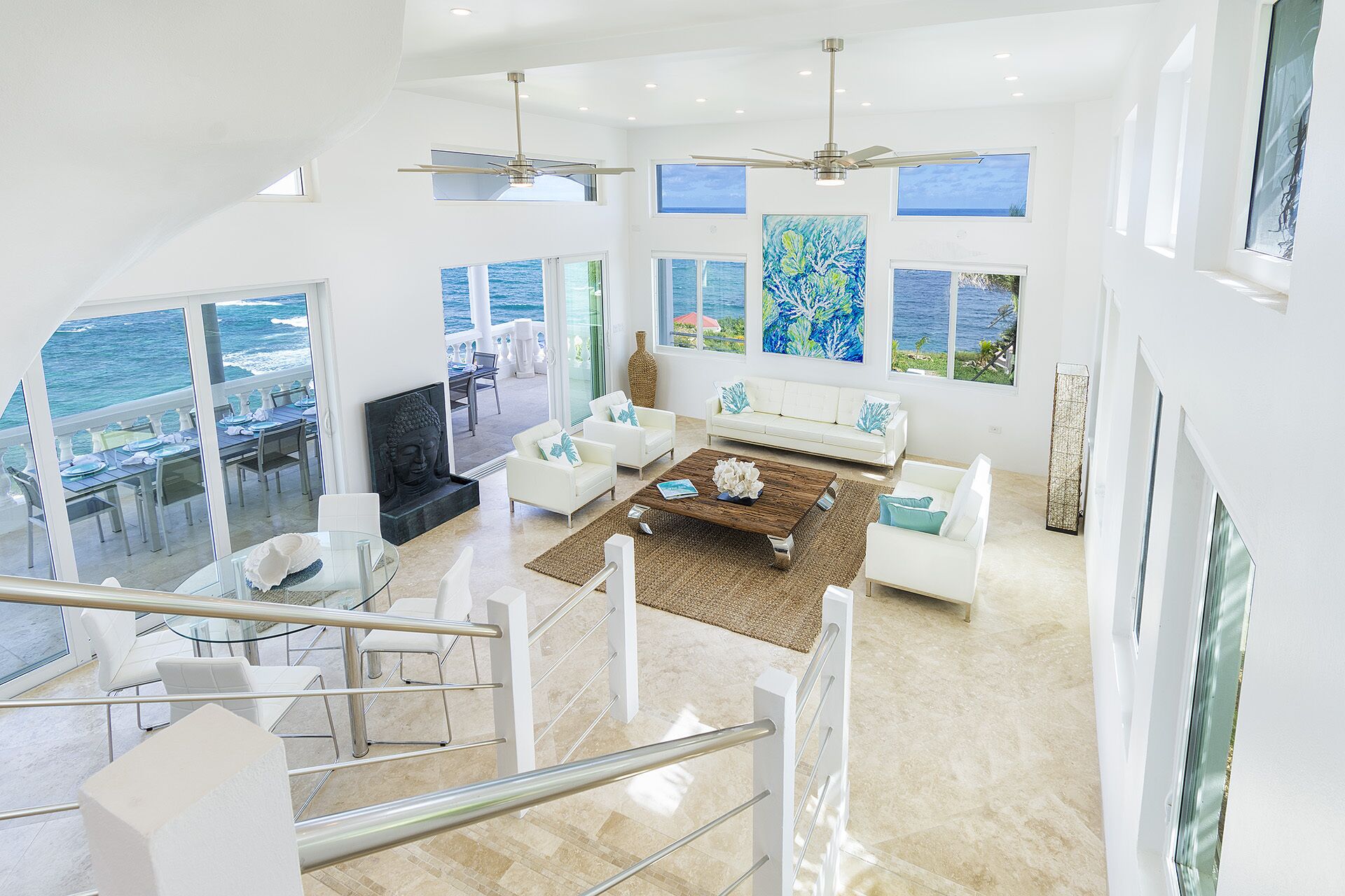 A spacious living area with a view of the ocean, white furniture, and a Buddha statue.