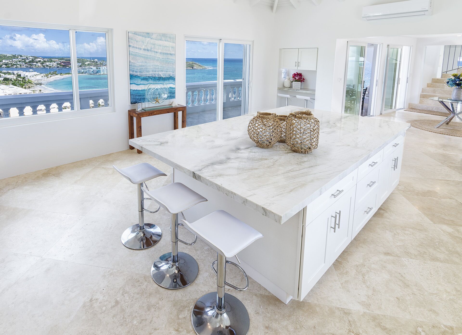 A modern kitchen with a large island, white cabinetry, and a view of the ocean.