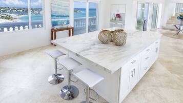 A modern kitchen with a large island, white cabinetry, and a view of the ocean.