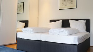 A neatly made bed with white linens and pillows, a dark headboard, and a framed artwork on the wall.
