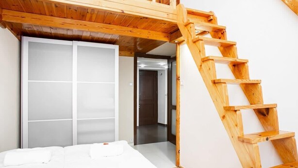 Un dormitorio con una escalera de madera que conduce a un altillo, una cama con ropa de cama blanca y un armario con puerta corredera.