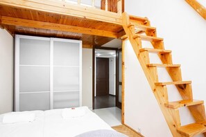 A bedroom with a wooden ladder leading to a loft area, a bed with white bedding, and a sliding door closet.